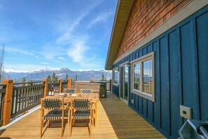 Una terraza de madera con una mesa y sillas, con vistas a un paisaje montañoso.