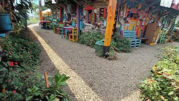 A colorful outdoor seating area with tables and chairs, surrounded by plants and a gravel path.