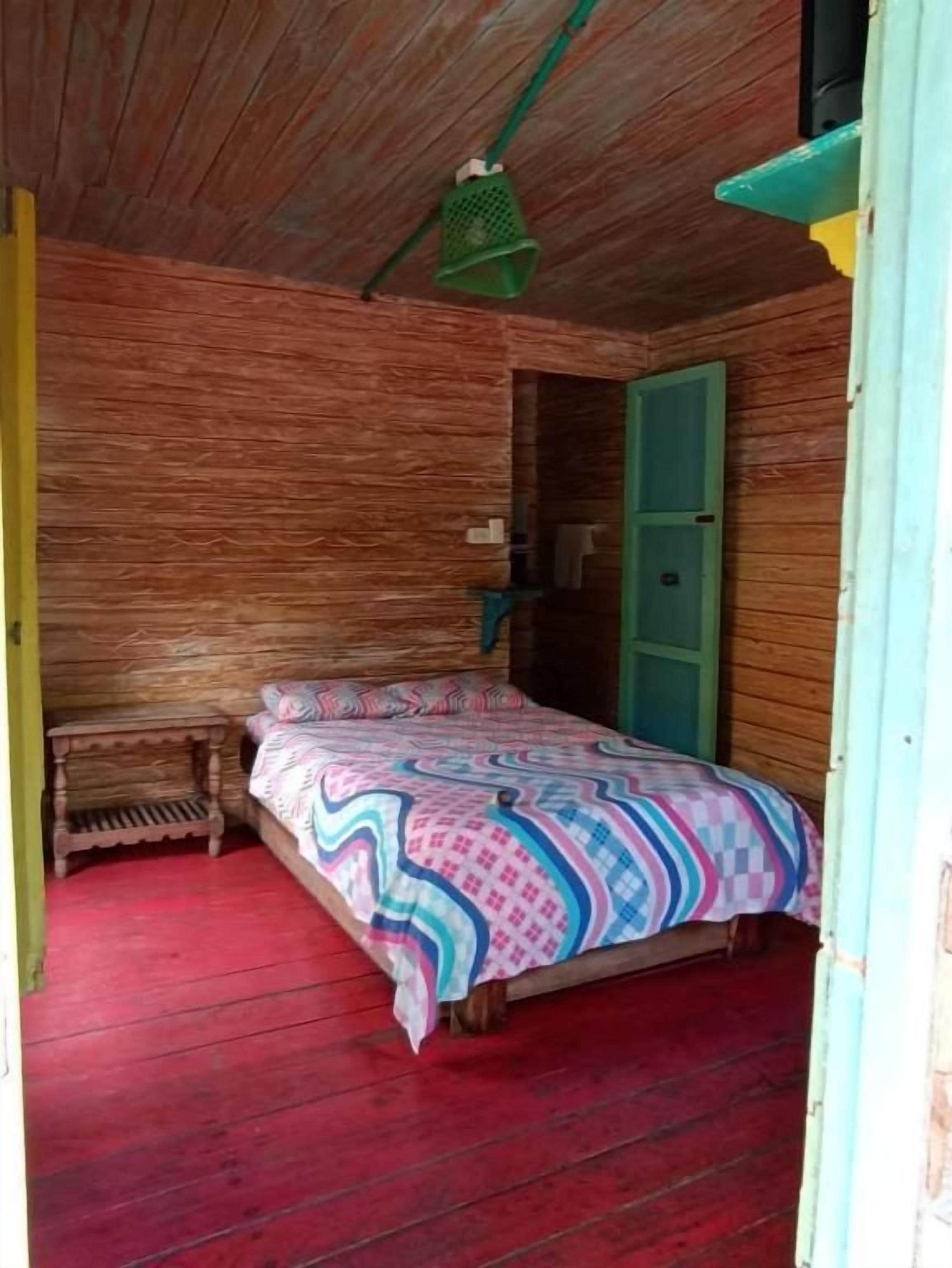 Una habitación de madera con una cama, una puerta verde y un pequeño banco.