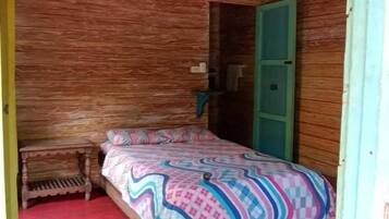 Una habitación de madera con una cama, una puerta verde y un pequeño banco.