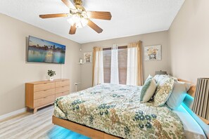 Ein Schlafzimmer mit einem Bett, einer Holzkommode, einem Deckenventilator, einem Fernseher und Bildern an den Wänden.