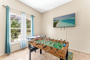 Une pièce avec une table de baby-foot, une fenêtre avec des rideaux et un téléviseur fixé au mur.