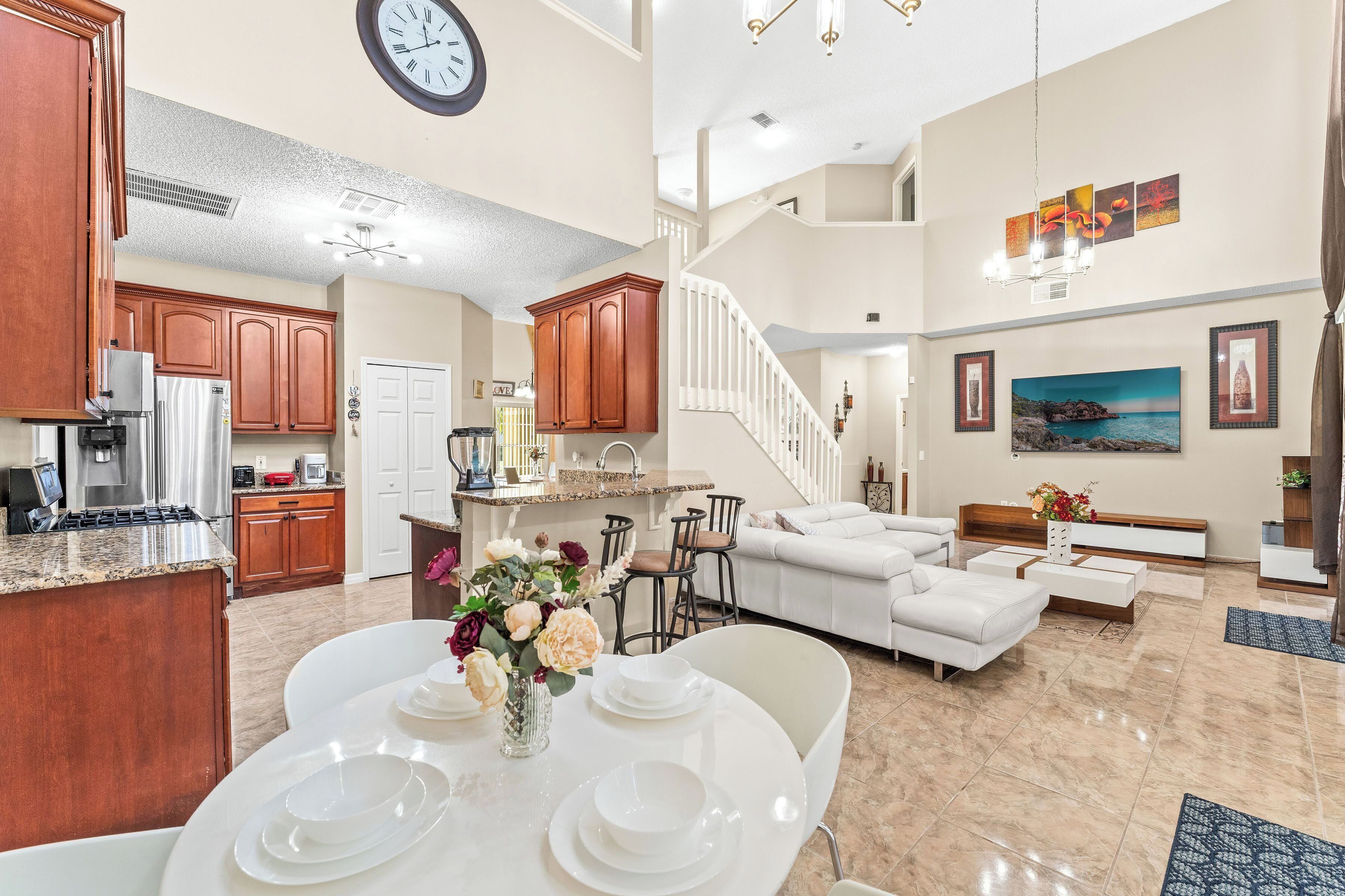 A spacious living area with a dining table set for four, a kitchen with modern appliances, and a staircase leading to an upper level.