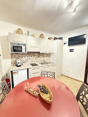 Una cucina compatta con forno a microonde, lavello e TV a schermo piatto fissata alla parete.