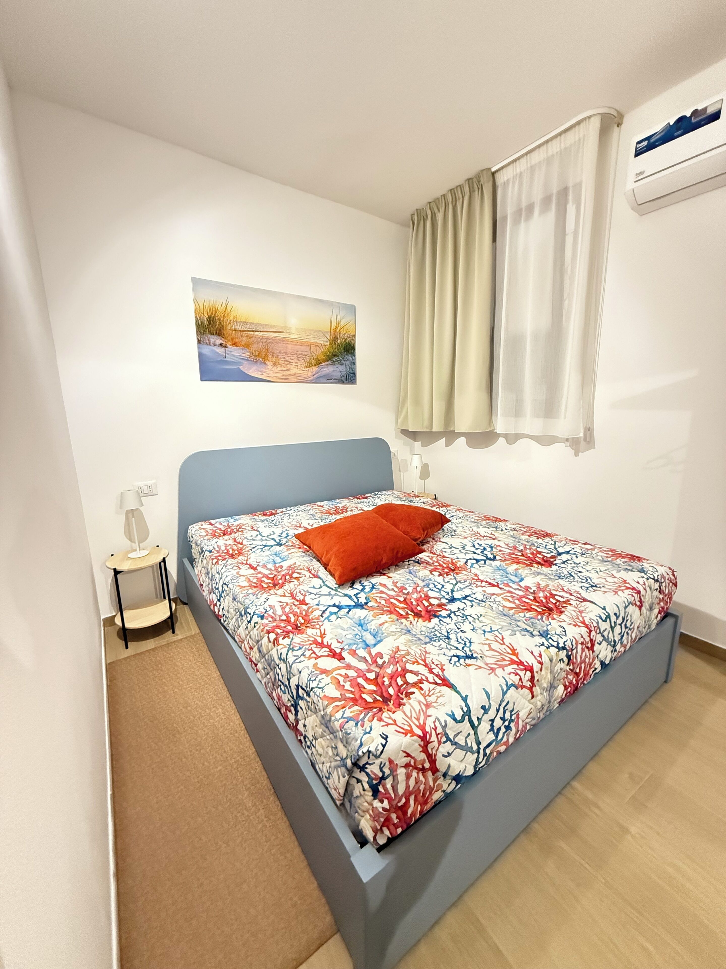 Una camera da letto con un letto, un comodino, una lampada, un quadro e un condizionatore d'aria.