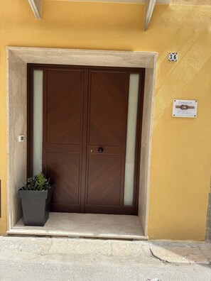 A double wooden door with a glass panel, a potted plant, and a sign with the number 36 on a yellow wall. - Cozy studio in the historic center of Trapani (Trapani)