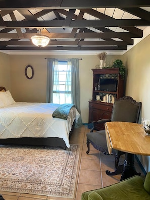 Un dormitorio con una cama, una silla de madera, una mesa, una estantería y una ventana con cortinas.