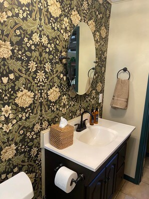 Ein Badezimmer mit blumigem Wandpapier, einem weißen Waschbecken, einem Spiegel, einem Handtuchhalter und einem Toilettenpapierhalter.