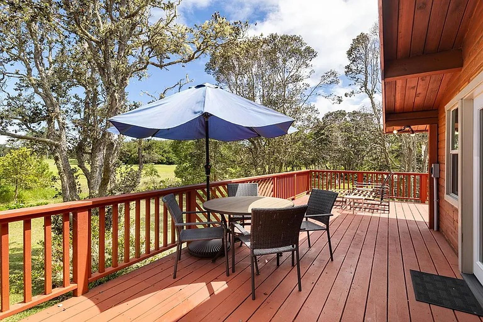 Une terrasse en bois, aménagée avec du mobilier d’extérieur, notamment une table et des chaises, et un grand parasol pour créer de l’ombre.