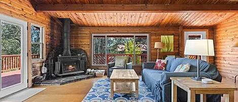 A cozy cabin interior with a fireplace, wooden walls, a sofa, and a ceiling fan.