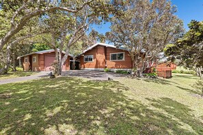 A two-story wooden cabin with a covered porch, surrounded by trees and a well-maintained lawn. - Cedar Log Home, Restful Haven, Couples Hideaway and Adventurous Family Basecamp. (Volcano)