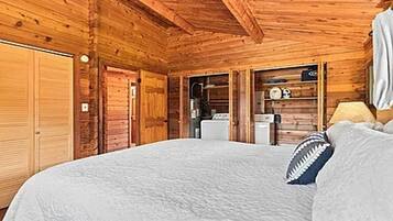 A log cabin bedroom with a bed, a wooden wardrobe, and a small kitchenette.