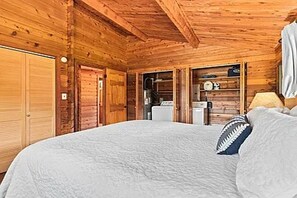 Un dormitori de cabana de fusta amb un llit, un armari de fusta i una cuineta petita.
