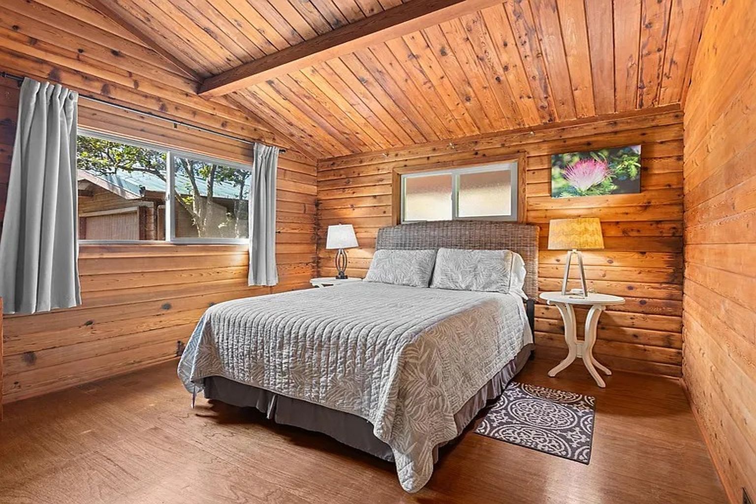 Une chambre à coucher située dans une cabane en bois, avec un lit, des tables de chevet, une fenêtre et une vue sur l’extérieur.