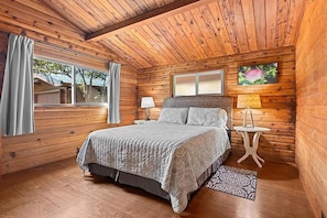 A wooden cabin bedroom with a bed, nightstands, a window, and a view of the outdoors. - Cedar Log Home, Restful Haven, Couples Hideaway and Adventurous Family Basecamp. (Volcano)