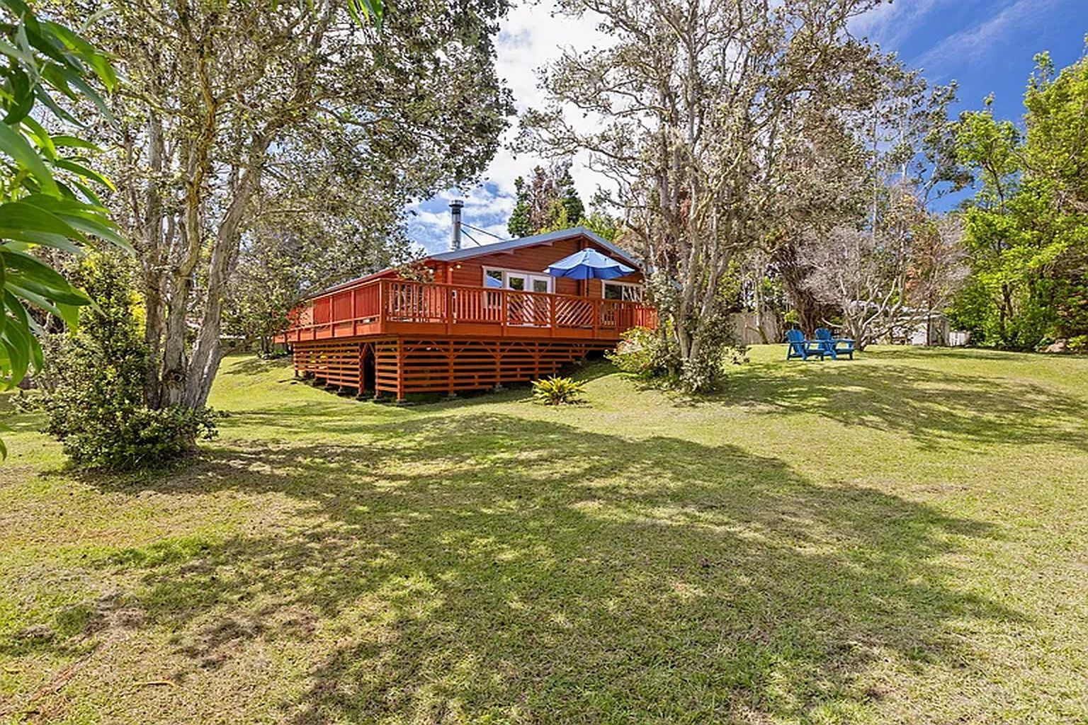 A wooden cabin with a deck, surrounded by trees and grass.