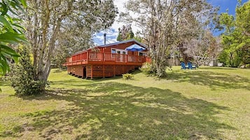 A wooden cabin with a deck, surrounded by trees and grass.