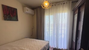 A bedroom with a single bed, a hanging light fixture, a painting on the wall, and a window with curtains. - Perfect chalet for rent North coast porto golf marina (Marsa Matrouh Governorate)