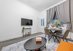 A modern living room with a flat-screen TV mounted on the wall, a dining table with chairs, and a small side table with a plant. - Modern ground floor apartment close to train station (Coatbridge)