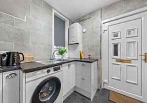 Een kleine keuken met een wasmachine, een spoelbak en een witte deur met een koperen knop.