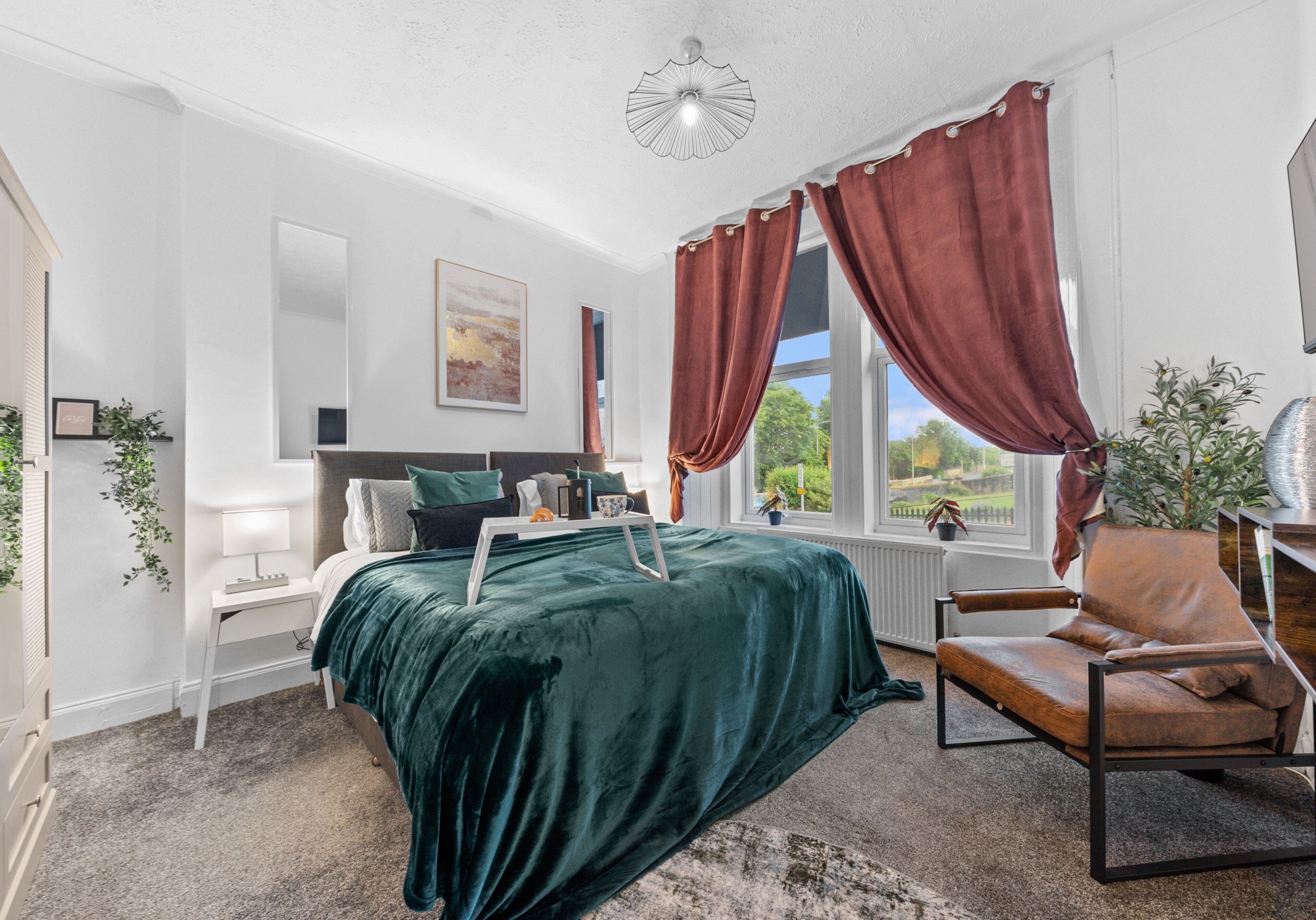 A modern bedroom with a bed, a chair, a window with curtains, a radiator, and a plant.
