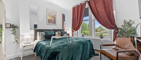 A modern bedroom with a bed, a chair, a window with curtains, a radiator, and a plant.