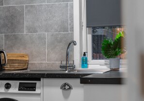 Een keuken met een moderne kraan, een houten snijplank, een plant in pot en een raam met uitzicht op groen.