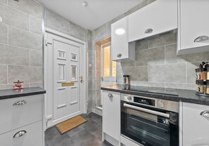 A modern kitchen with grey tiles, white cabinetry, a built-in oven, and a black countertop. - Modern ground floor apartment close to train station (Coatbridge)