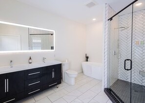 Un baño moderno con un espejo grande, un tocador negro, un inodoro y zona de ducha con mampara de cristal.