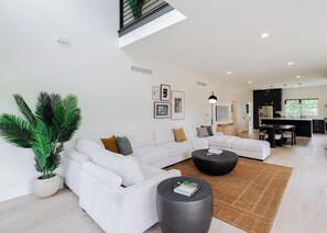 A modern living room with a sectional sofa, a coffee table, and a potted plant. - The Clubhouse | Ultimate Golf & Game House (Kansas City)