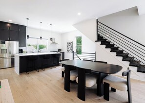 Una cocina moderna con una isla central, taburetes negros y una escalera con barandillas negras.