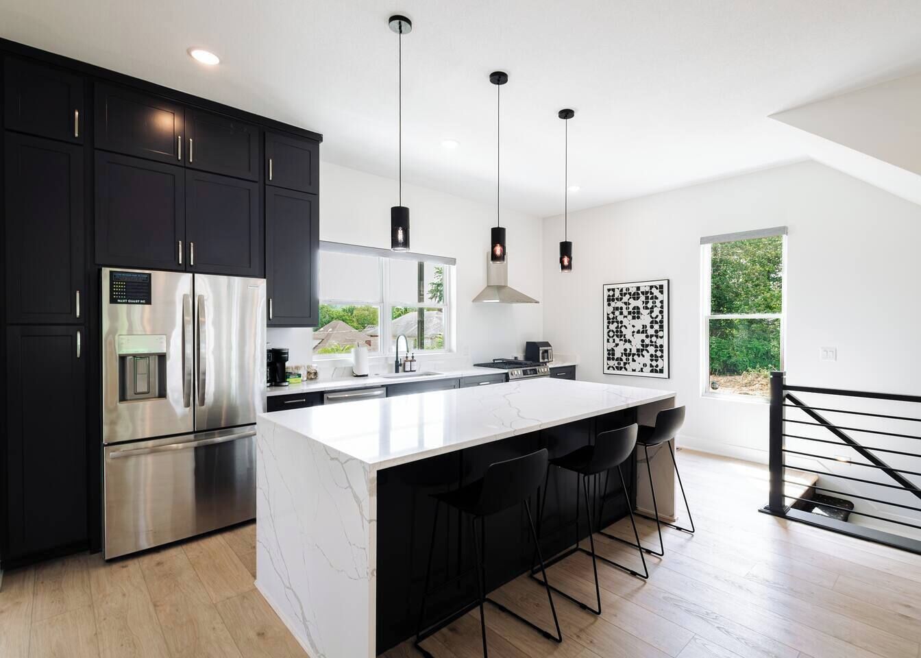 A modern kitchen with a large island, stainless steel appliances, and black bar stools.