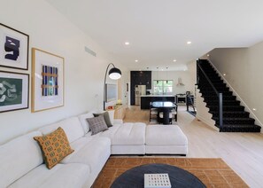 Un salon moderne avec un canapé d’angle, une table basse et un escalier menant à l’étage supérieur.