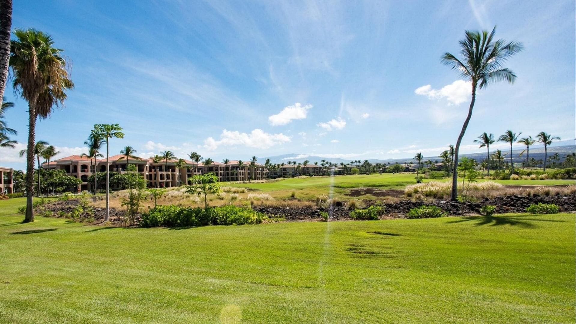 A golf course with a clubhouse, palm trees, and a clear sky.