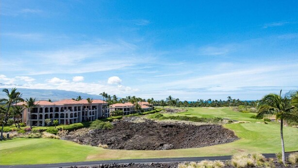 Un parcours de golf avec un grand cratère, des palmiers et un bâtiment doté de nombreux balcons.