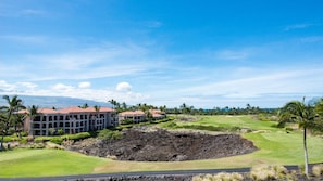 A golf course with a large crater, palm trees, and a building with multiple balconies.