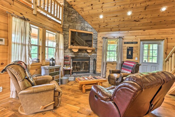 A cozy cabin interior with a stone fireplace, leather furniture, and wooden walls.