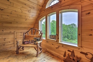 Interior de una cabaña con paredes de madera, un banco rústico de madera y ventanas amplias que dan a un bosque.