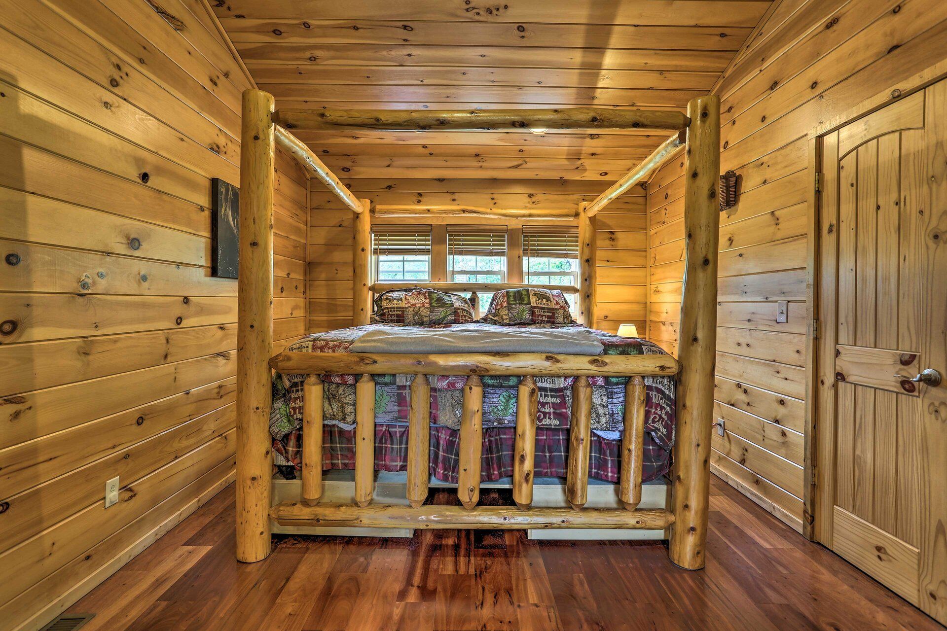 A wooden cabin room with a bed, a window, and a door.