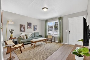 Un salon comprenant un canapé, une table basse, un fauteuil, une lampe sur pied et un téléviseur.