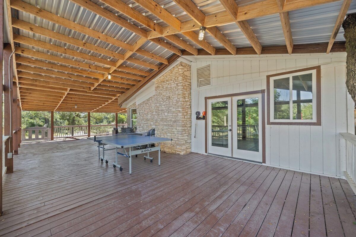 A covered outdoor area with a ping pong table, stone wall, and a door leading to a covered patio.