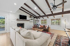 A spacious living room with a stone fireplace, a large sofa, and a ceiling fan. - Austin 5BR - Pool & Spa - Games - Indoor Fire (Austin)