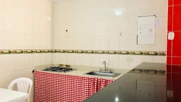 Una cocina compacta con estufa a gas, lavabo y mantel a cuadros rojos y blancos cubriendo la encimera.