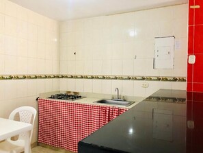 Een kleine keuken met een gasfornuis, spoelbak en een rode en witte geruit tafelkleed over het aanrecht.