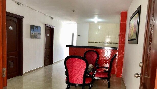 Un pasillo con una zona de comedor que incluye sillas rojas y piso de baldosas.