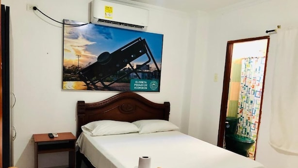 A hotel room with a bed, a nightstand, a wall-mounted air conditioner, and a poster. - Hotel Casa Martina Valledupar (Valledupar)