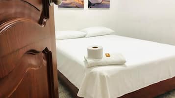 Habitación de hotel con puerta de madera, cama con ropa blanca y un rollo de papel higiénico sobre la cama.