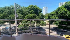 Un balcón con barandilla de metal, vista despejada a un estacionamiento y edificios al fondo.