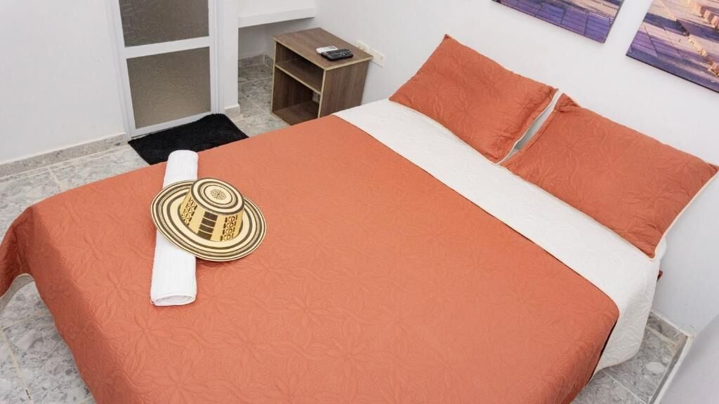 Una cama bien hecha con un edredón estampado, una toalla blanca enrollada y un cabecero decorativo.
