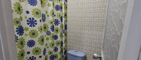 Een kleine badkamer met toilet, douchegordijn en betegelde wand.